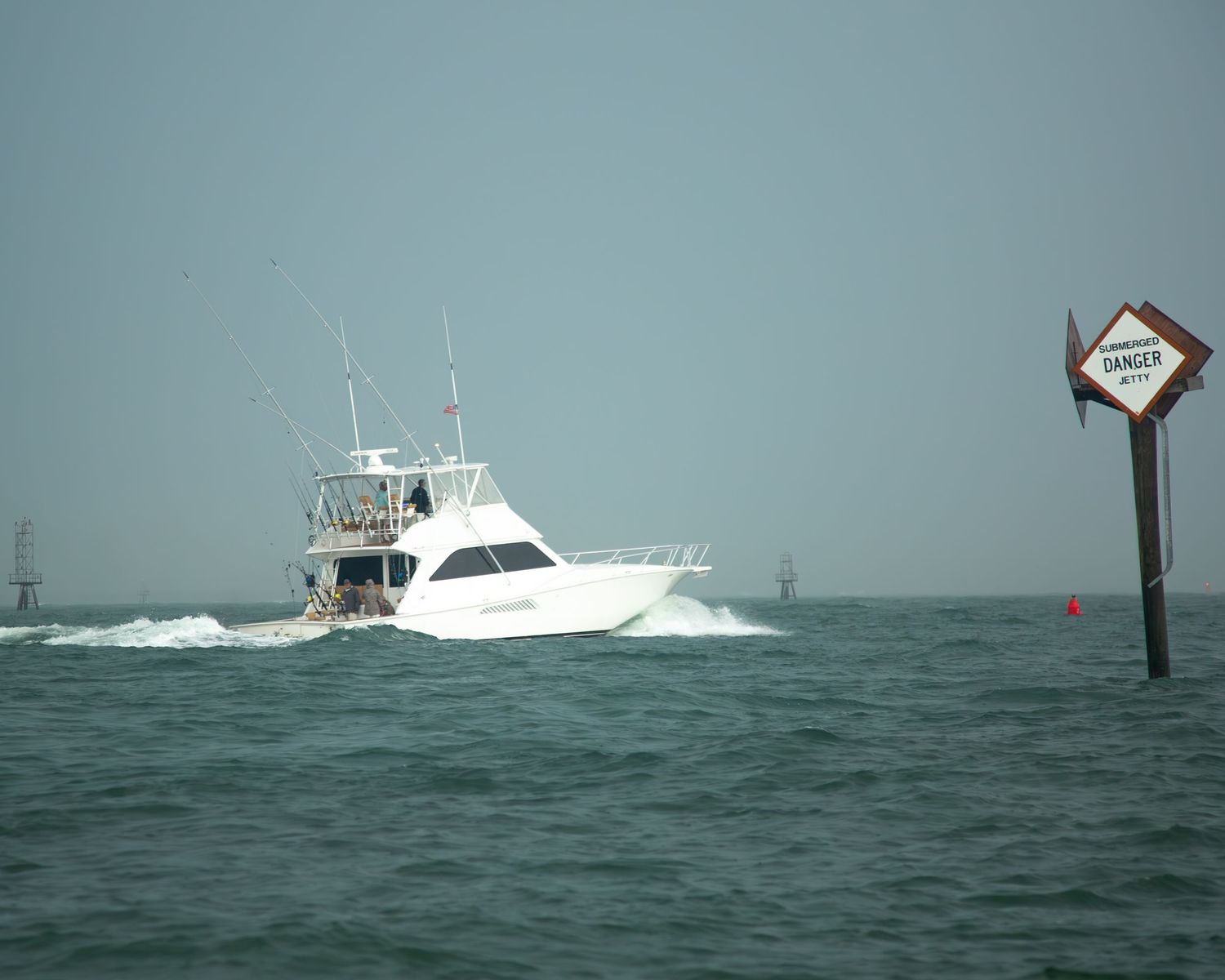 Large white sport fishing boat passing a channel marker in choppy seas.