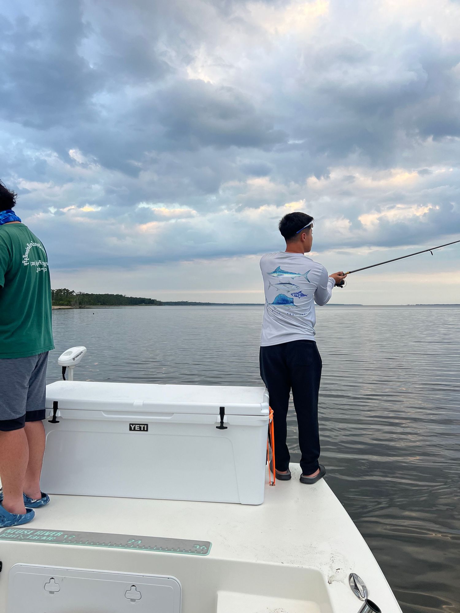 Anglers fishing from a boat on calm waters during sunset with cloudy skies.