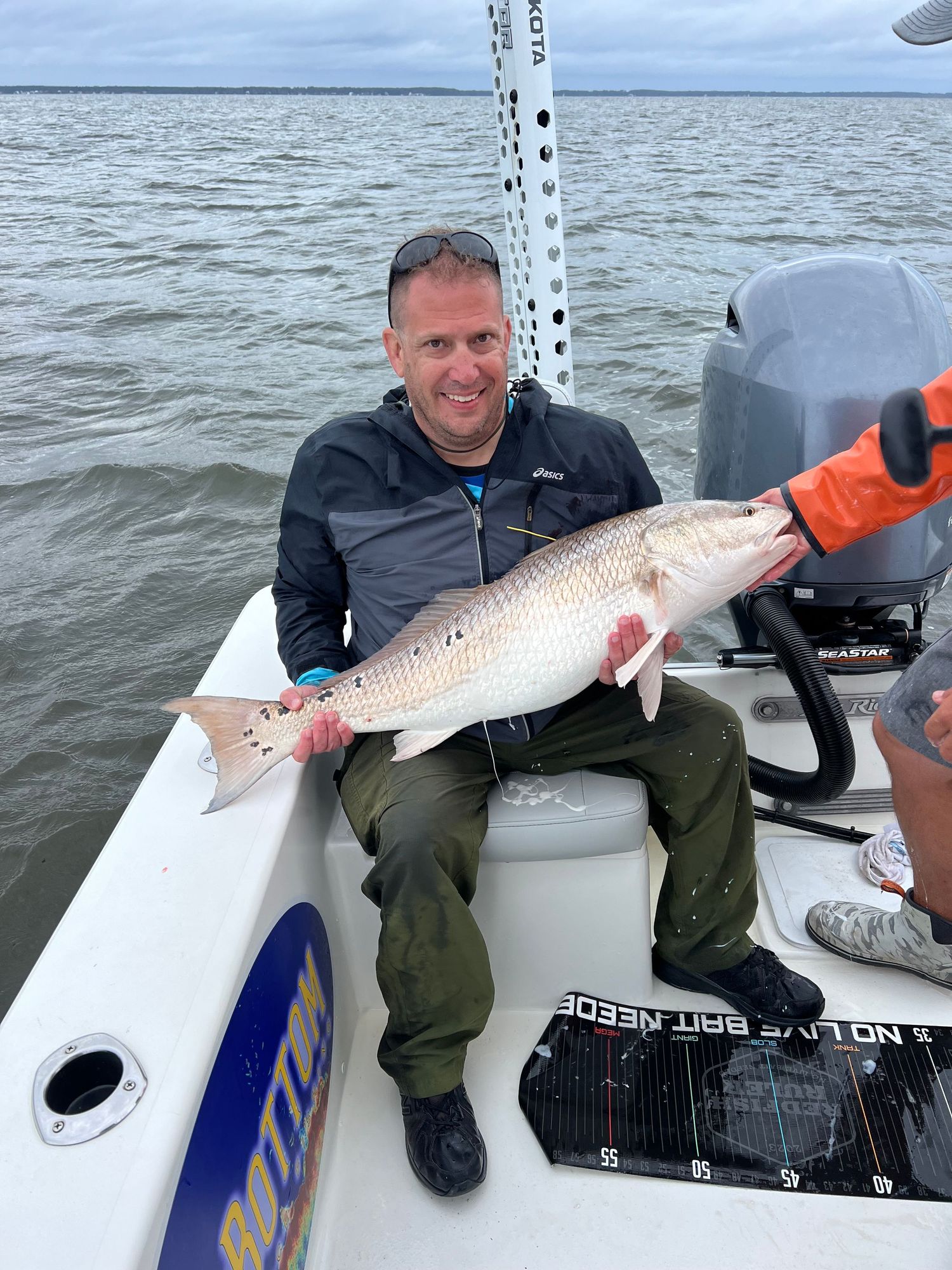 Recreational angler shows off a sizeable redfish catch while seated on a boat.