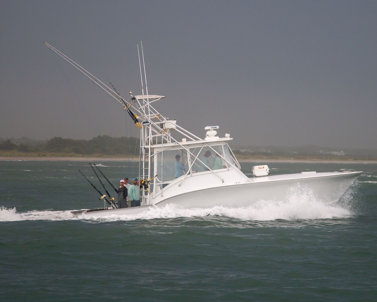 White sport fishing boat with fishing poles cutting through waves in coastal waters.