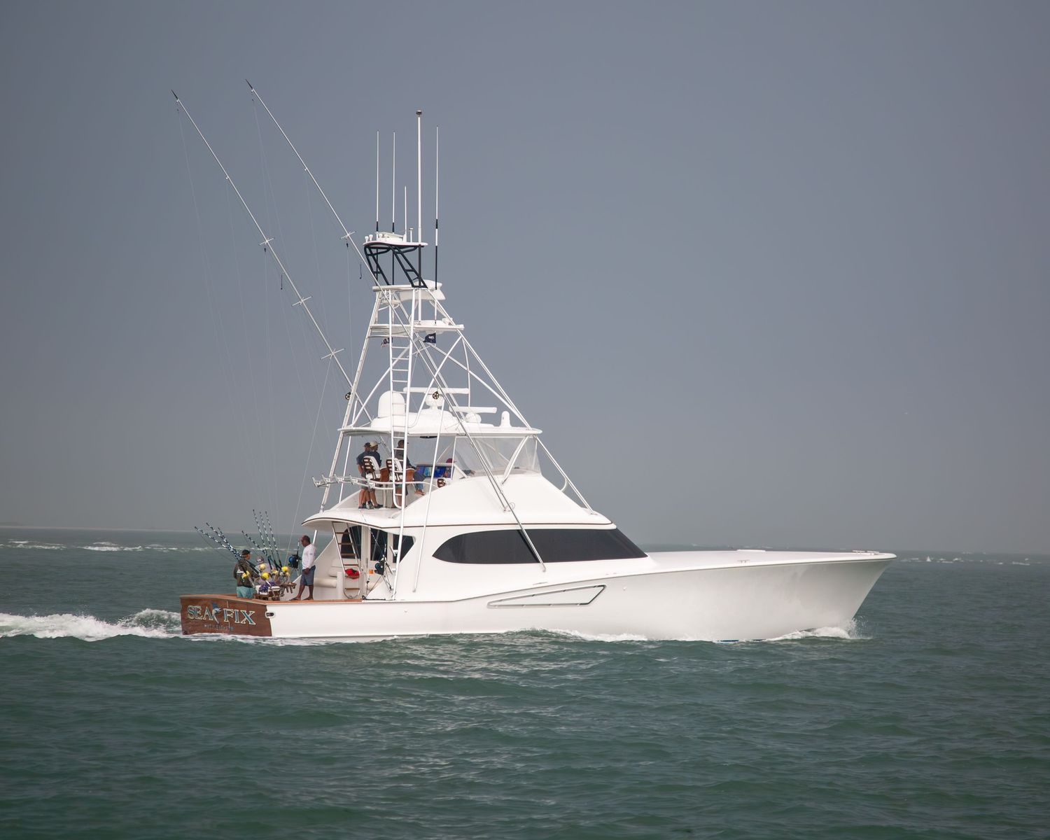 Large white sportfishing yacht creating wake while moving through rough seas.