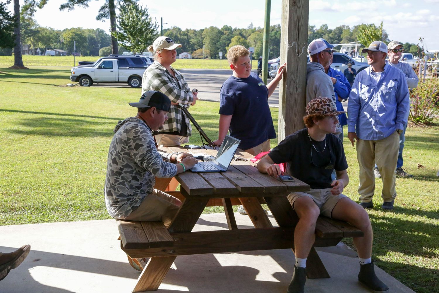 Group gathered at picnic table during outdoor fishing event.