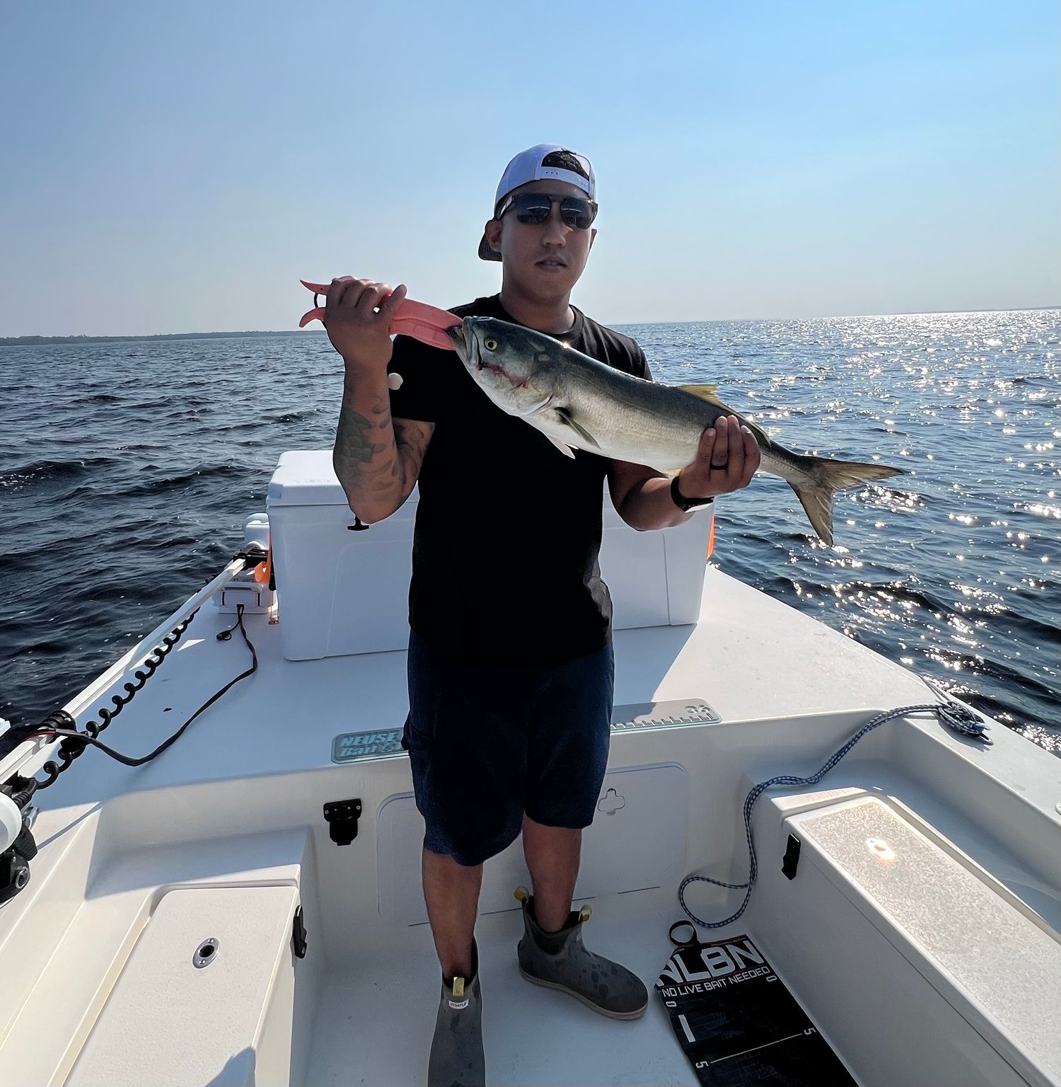 A person fishing on a boat catching fish under bright sunlight on a blue ocean.