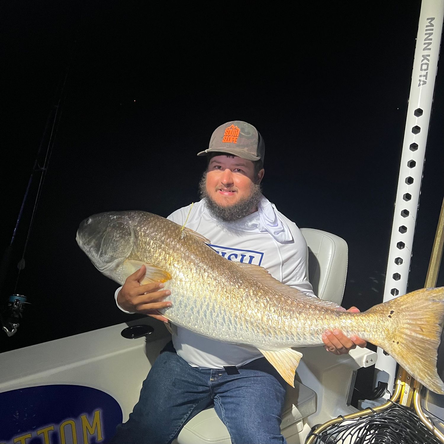 Angler on a boat proudly displays a large redfish catch during a successful fishing trip.