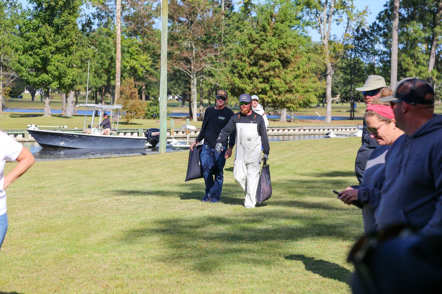 Tournament participants walking across grass field at outdoor fishing event.