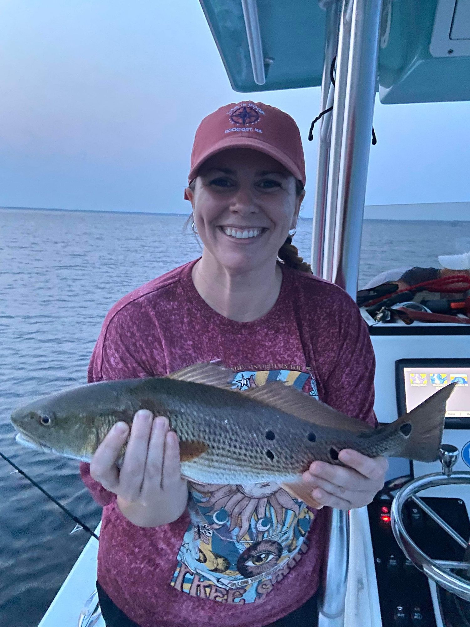 Angler displays fresh caught redfish on boat during evening fishing trip.