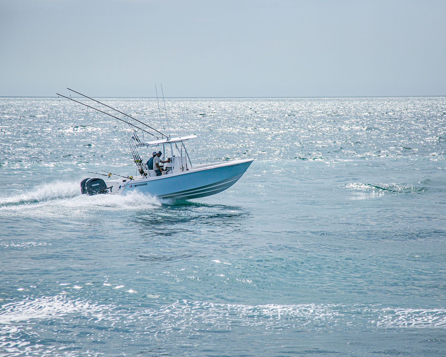 Teal center console fishing boat speeding across sparkling open ocean waters on a clear day.