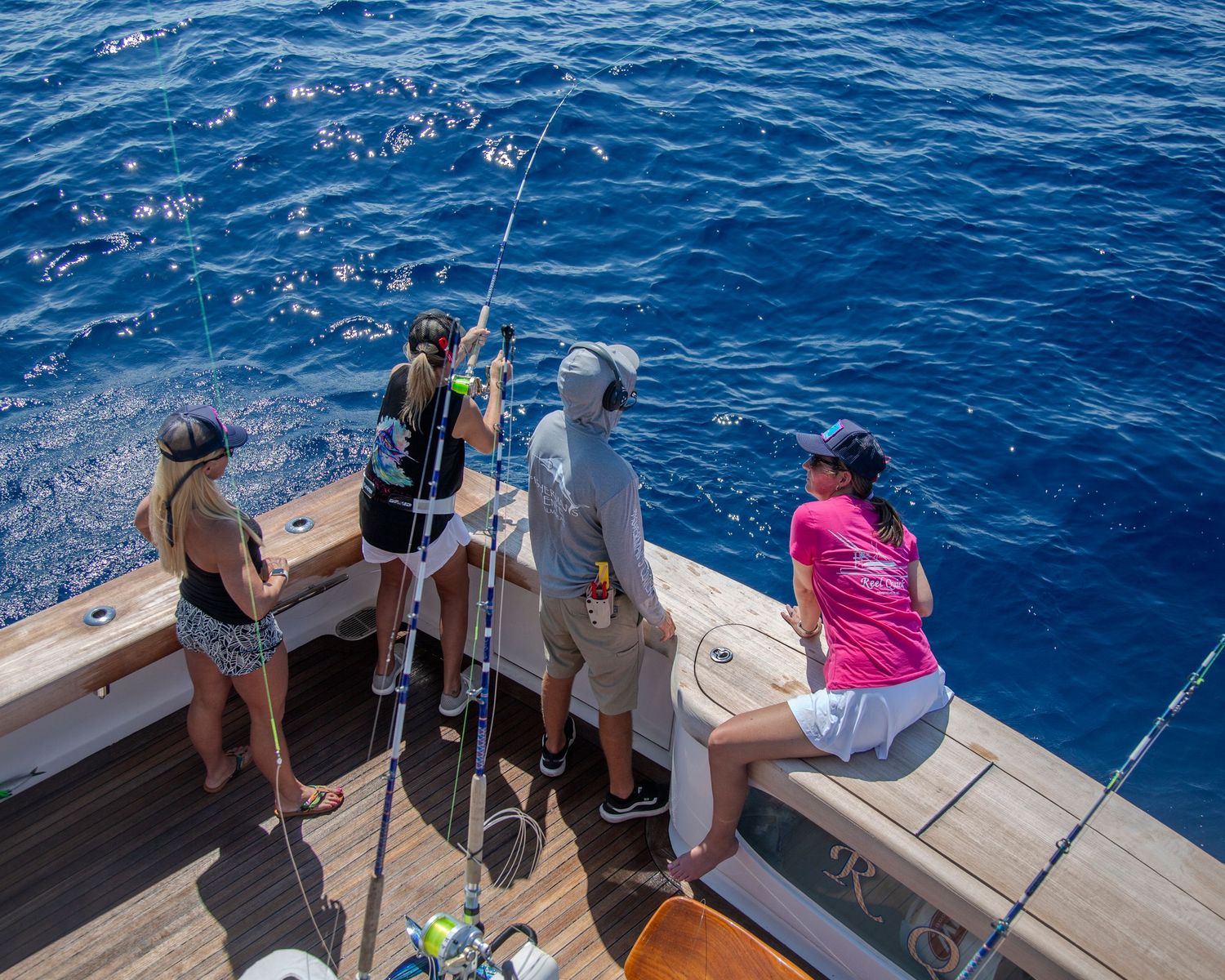 Group of people deep sea fishing off the stern of a luxury yacht on calm blue ocean waters on a sunny day.