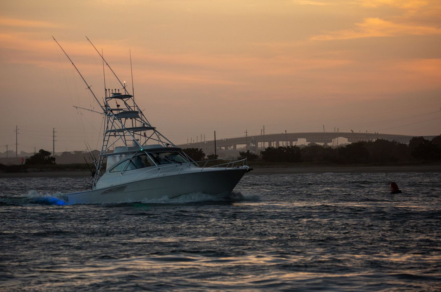 Luxury sport fishing yacht silhouetted against dramatic orange sunset sky.