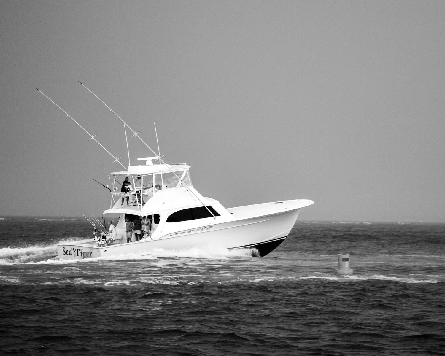 Black and white image of fishing yacht cutting through ocean waves at high speed.