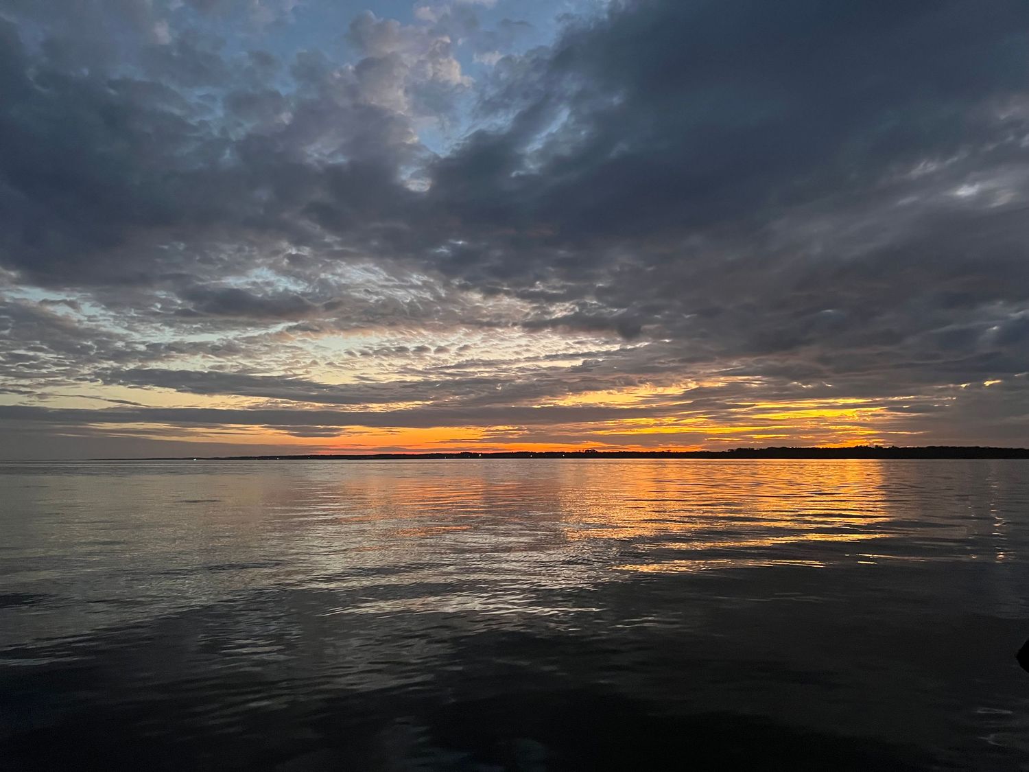 Wide view of stormy clouds at dusk reflecting on dark lake waters with an orange horizon.