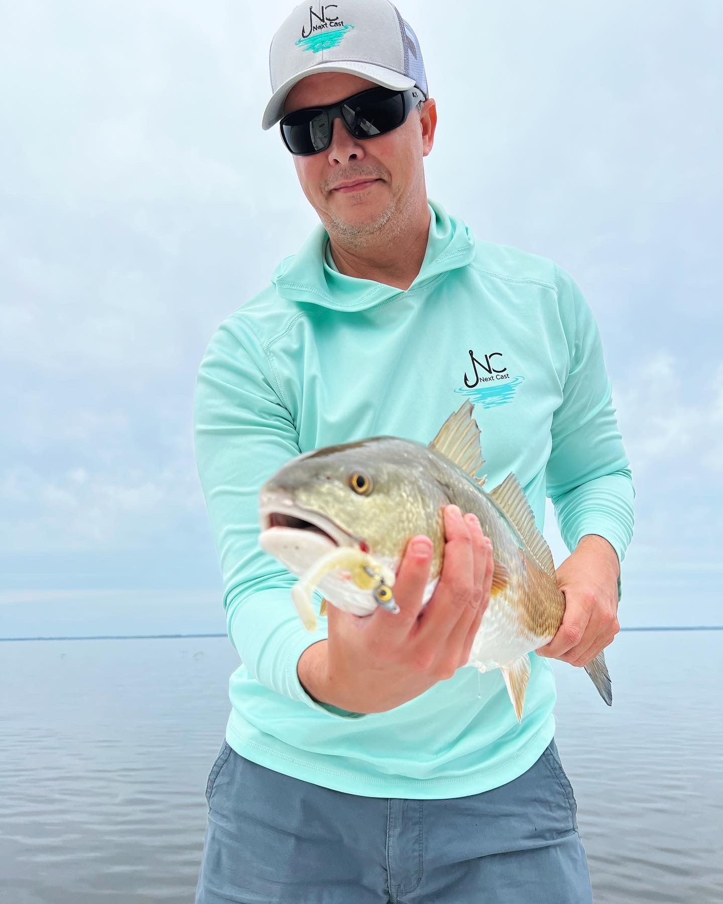 Angler in mint-colored shirt displays a freshly caught fish on a boat during daytime fishing trip.