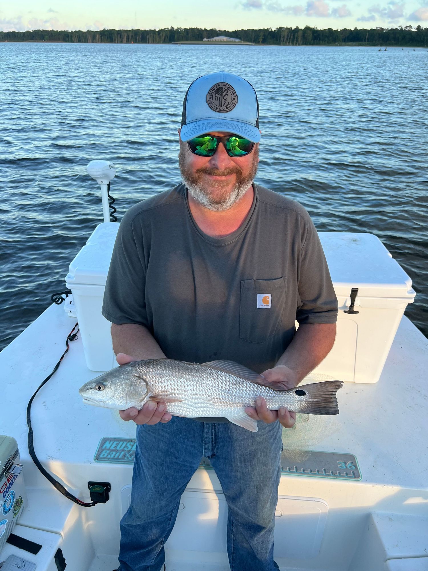 Fisherman displays fresh caught drum fish while boating on calm waters.
