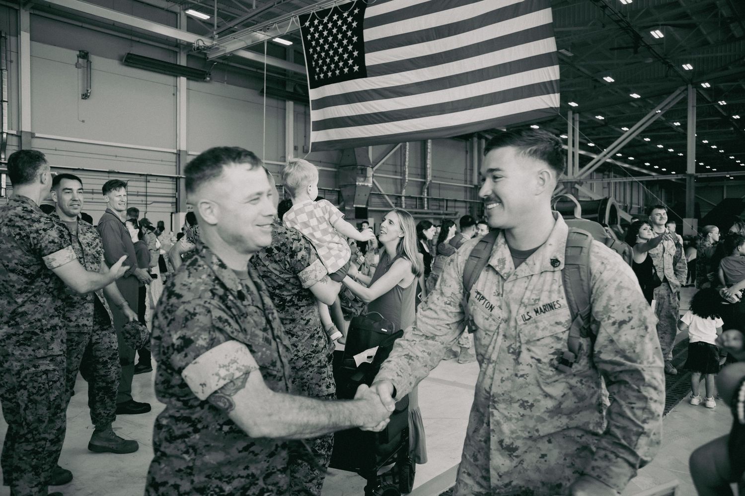 Military service members gather in a room with American flag for a welcome home celebration.