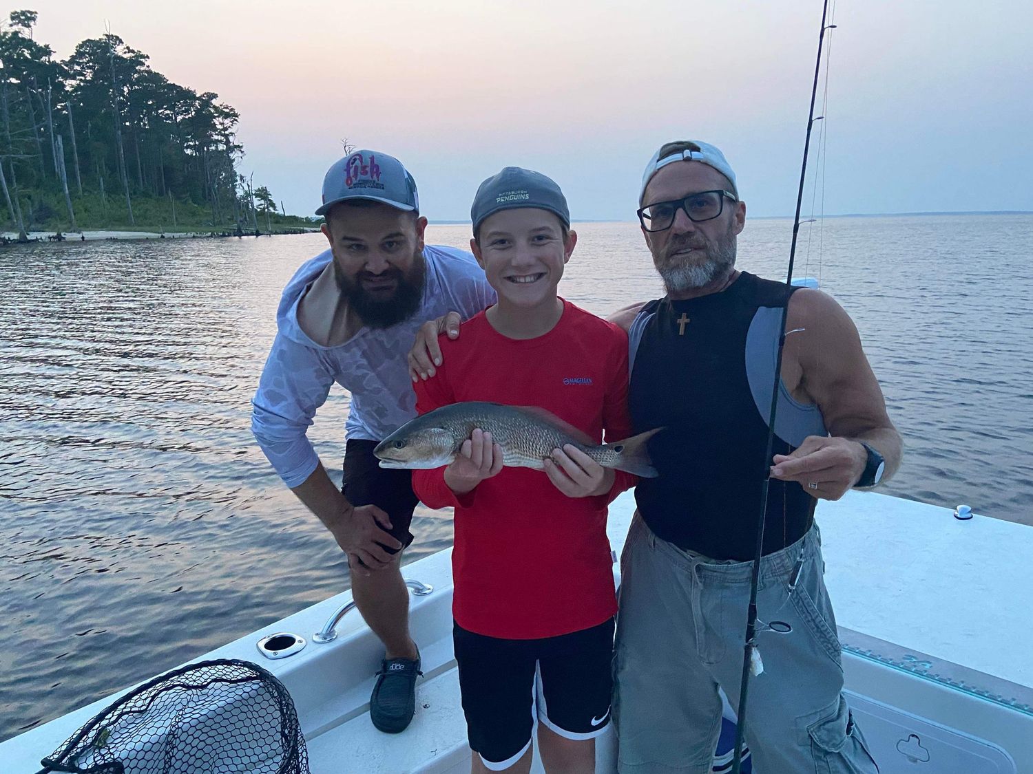 Three people on a boat display their catch during a sunset fishing trip.