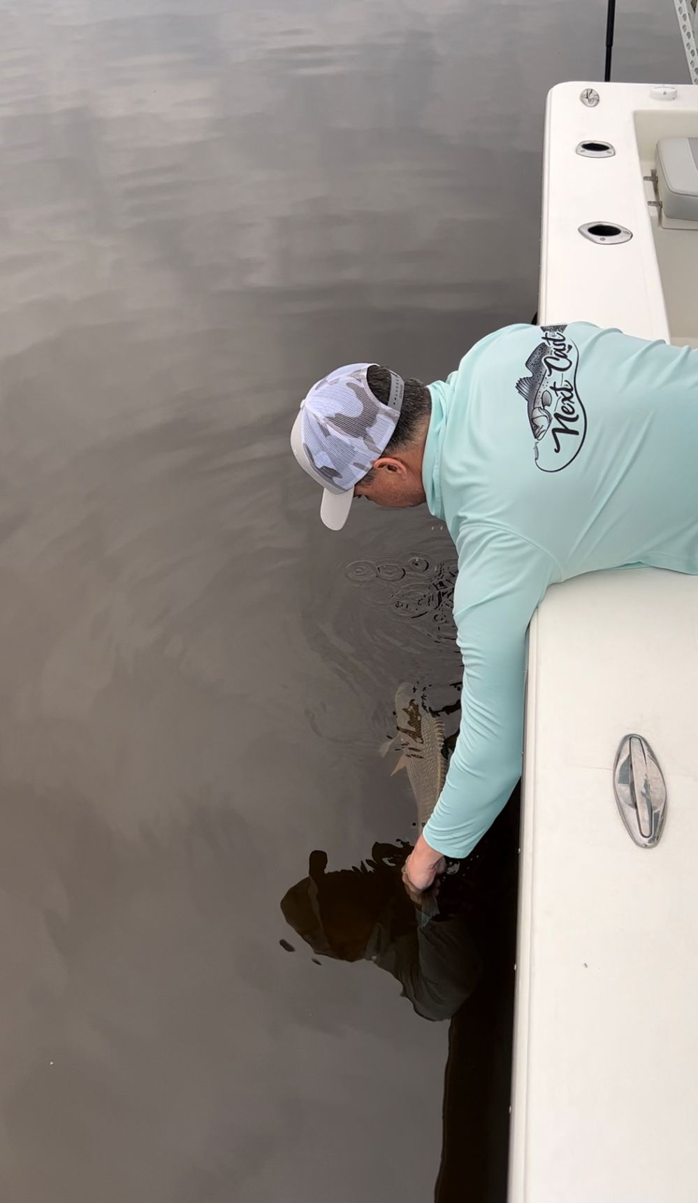 Side view of someone in light blue shirt leaning over boat edge handling fishing equipment.