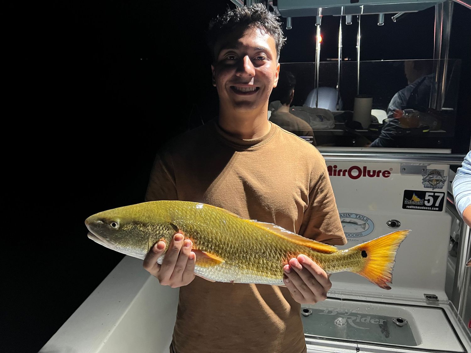 Proud angler shows off golden redfish catch at night on fishing boat.
