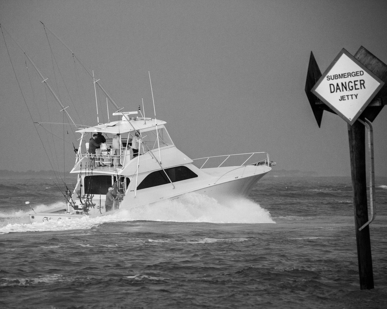 Fishing boats pass danger markers while navigating through stormy ocean conditions.