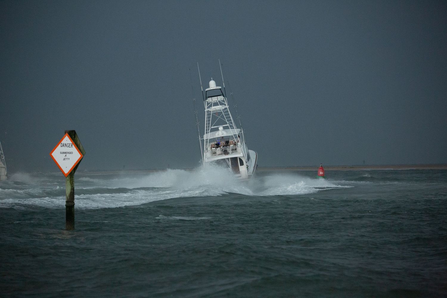 Fishing boats navigate through turbulent waters past warning markers in stormy conditions.