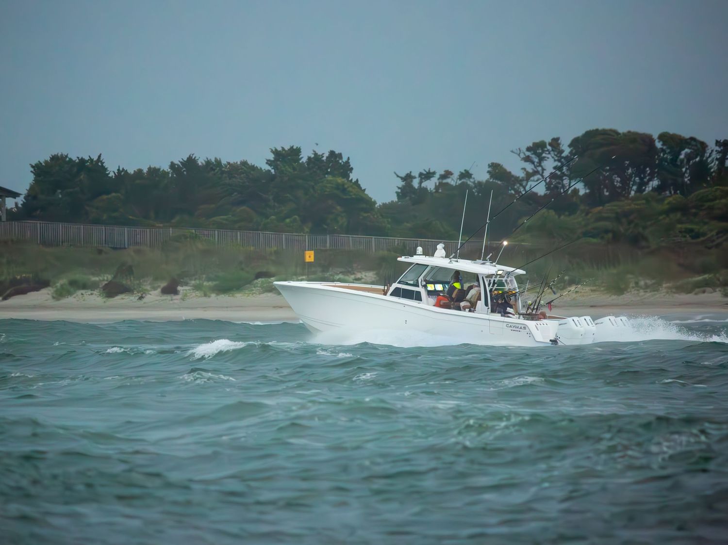 Multiple fishing boats navigate coastal waters near a tree-lined shore.