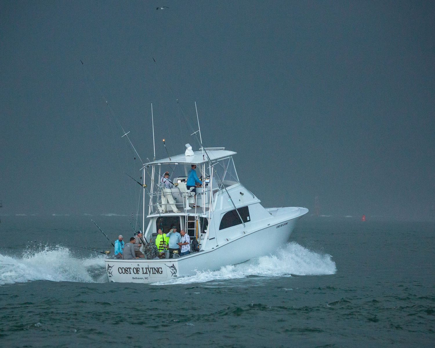 Charter fishing boat with outriggers creates wake while navigating through stormy conditions.