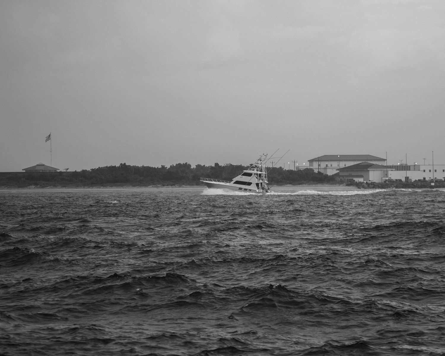 Black and white seascape showing boats on rough waters near the shoreline.