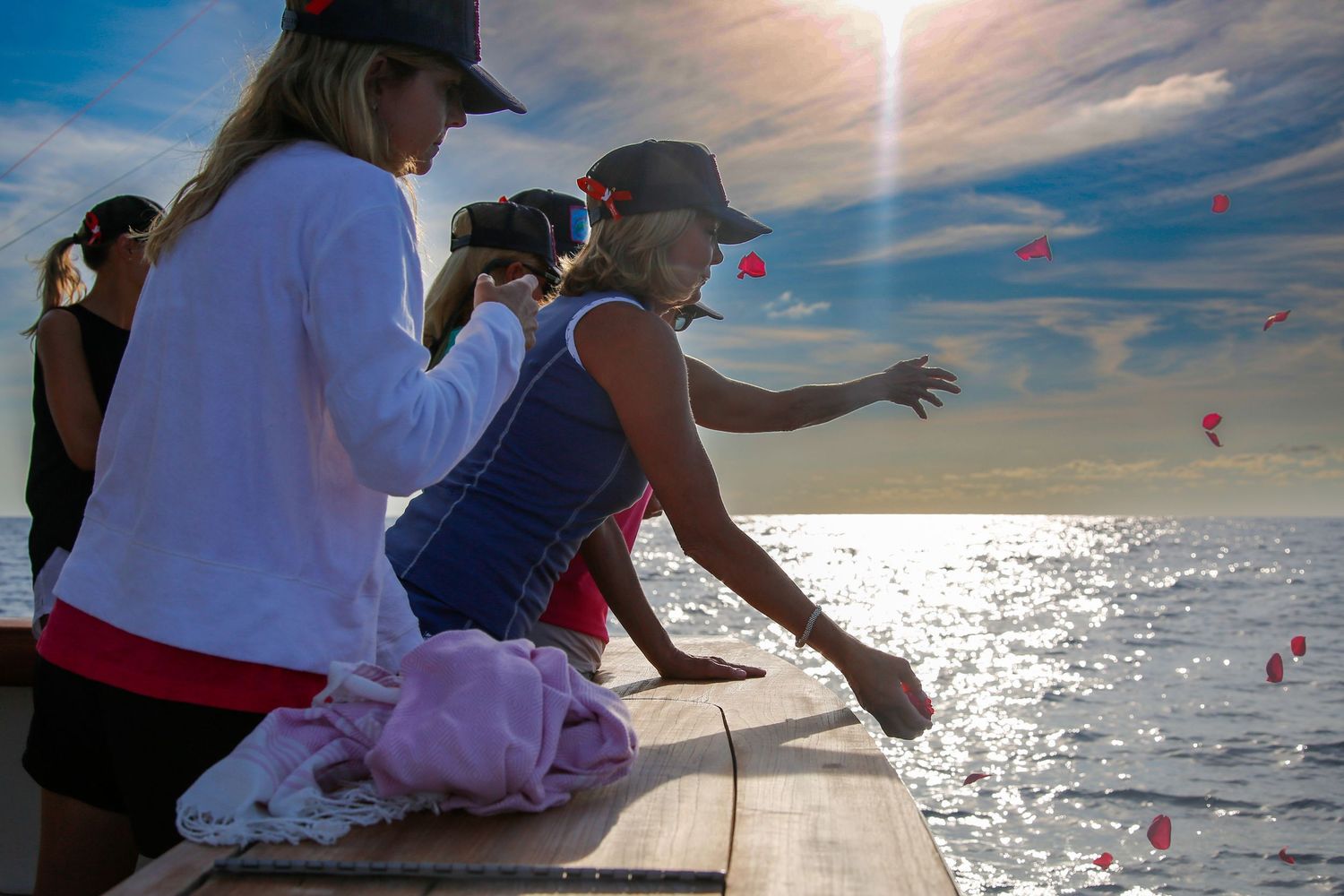 People scattering flower petals into the ocean from a boat deck at sunset, a meaningful memorial ceremony at sea.
