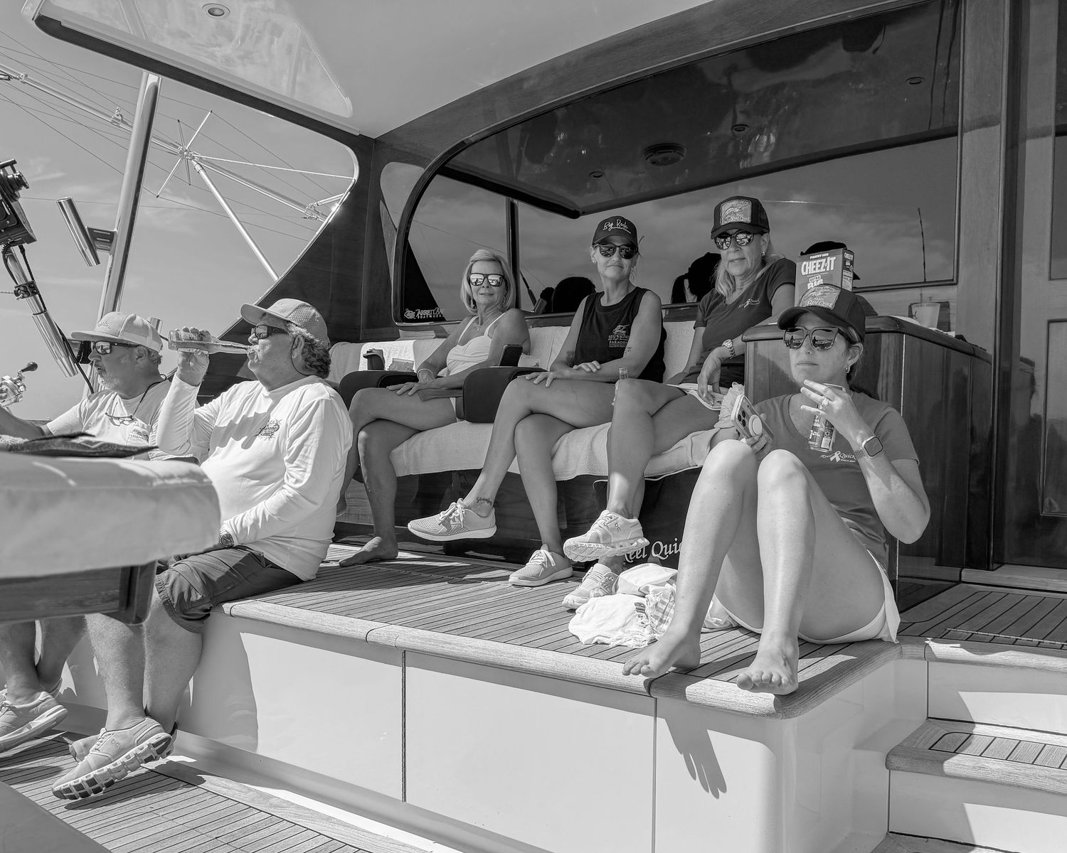 Black and white photo of a group of people relaxing on the deck of a sailboat on a sunny day.