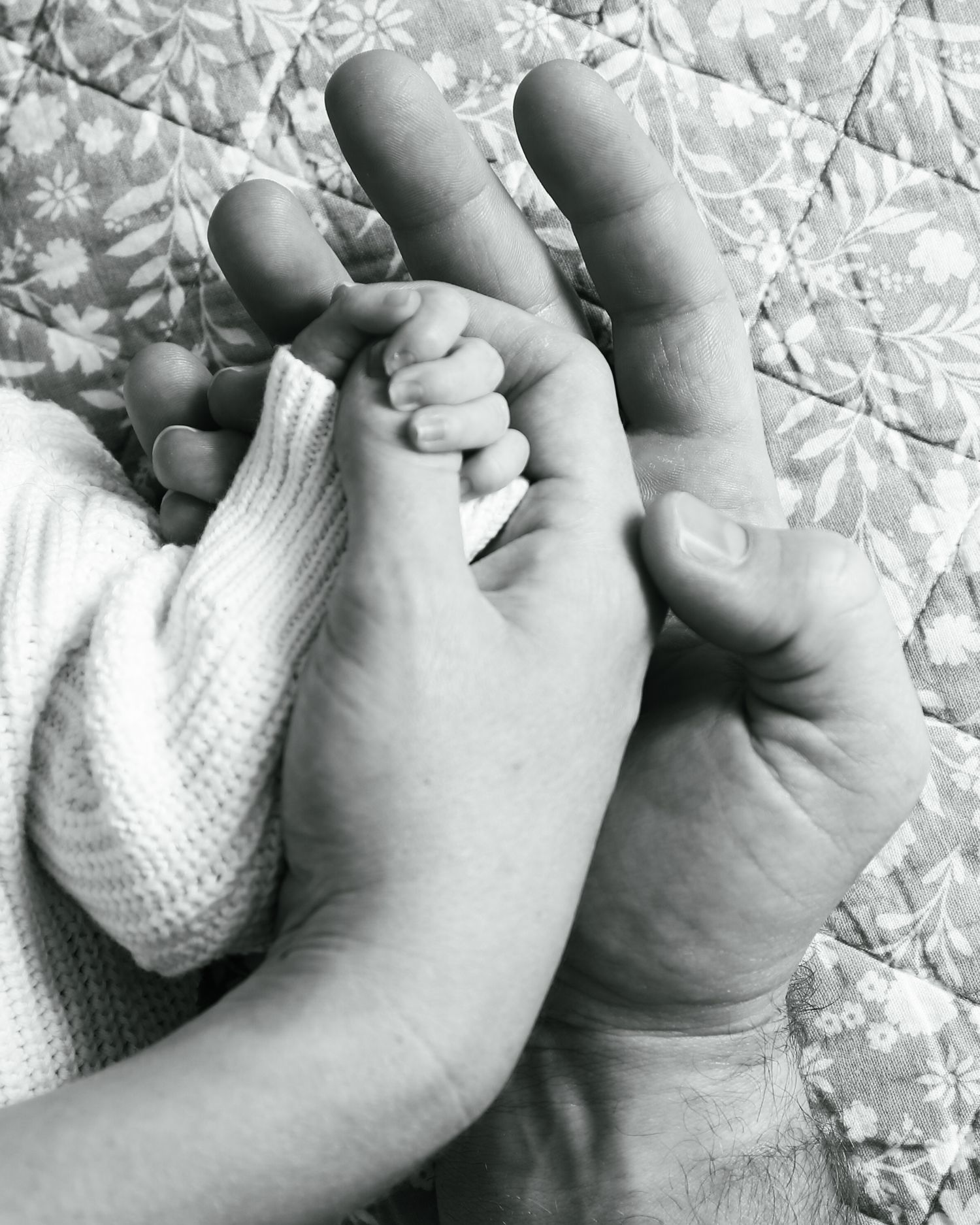 Black and white photo of a newborn baby's tiny hand grasping an adult's finger, symbolizing new life and parental love.