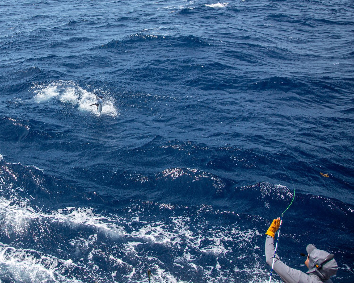 Fishing line trailing into deep blue ocean waves from a boat with a yellow lure visible above the water.