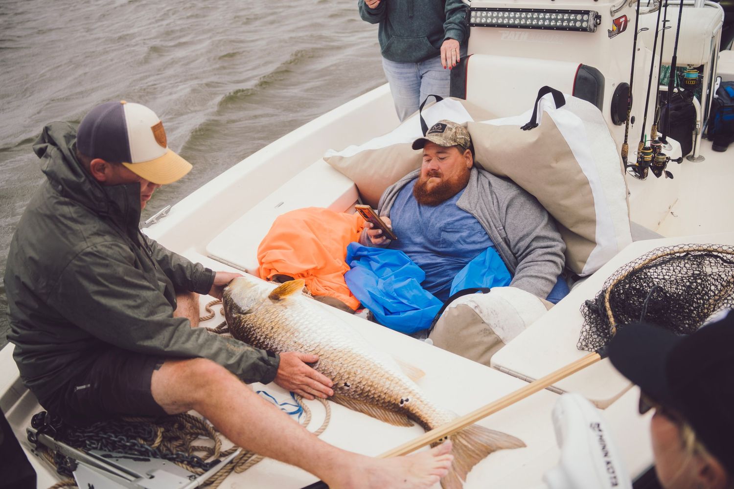 Men on a fishing boat holding a large fish catch on a cloudy day near open water.