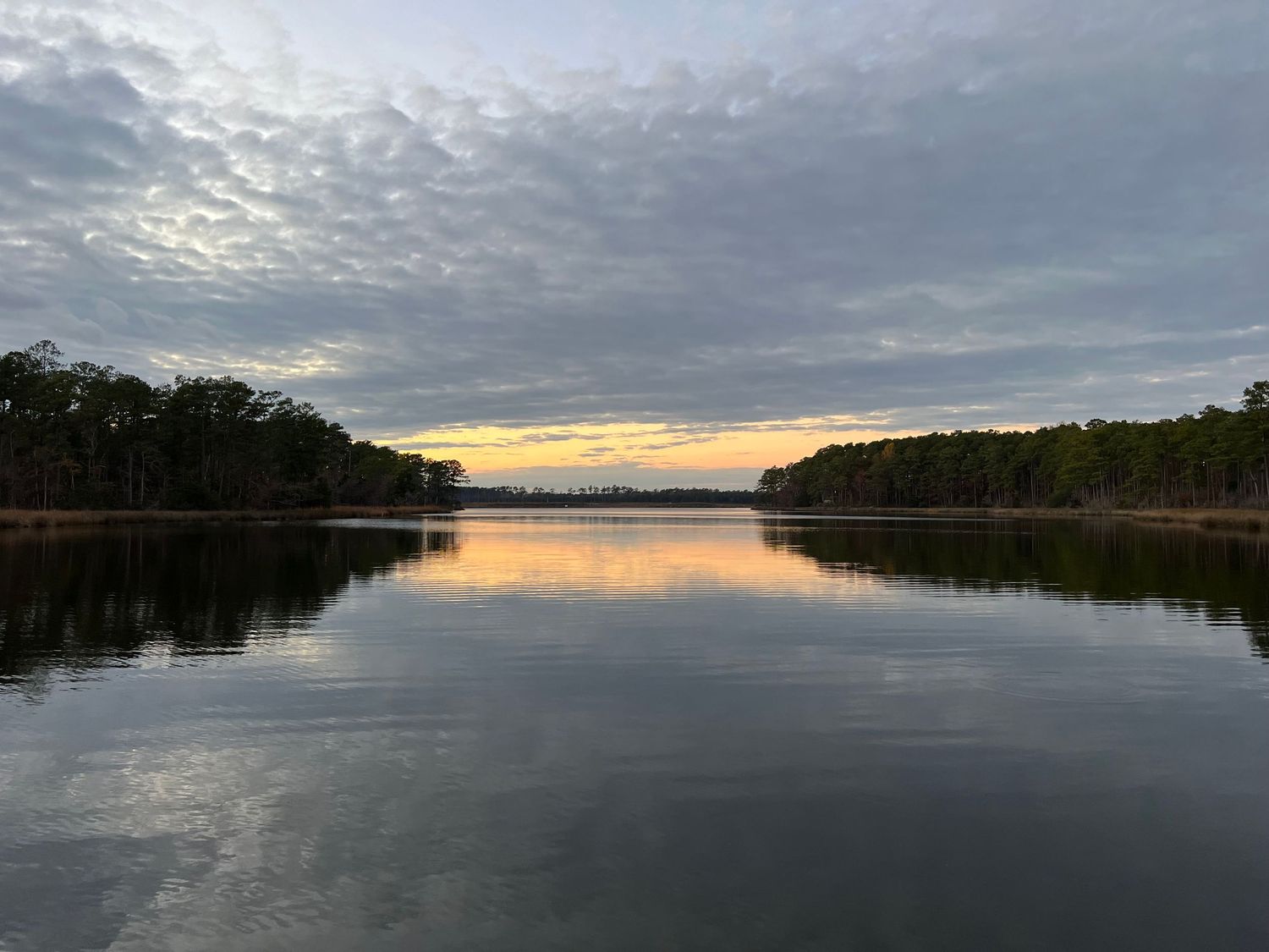 Serene lake landscape at sunset with cloudy skies reflected in calm waters.