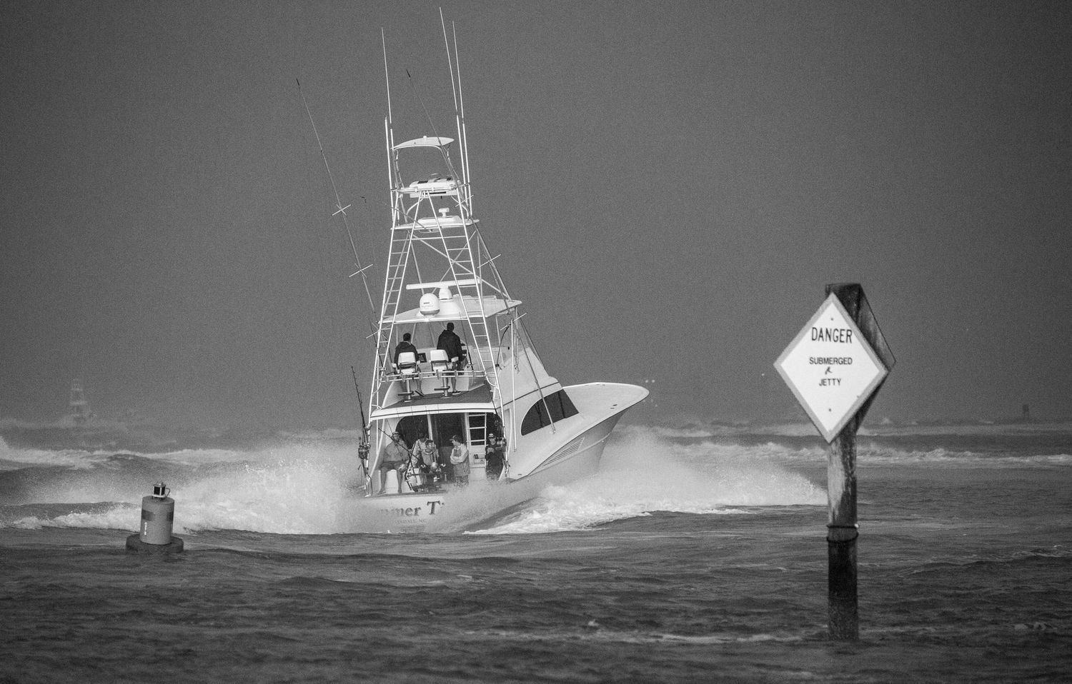 Boats maneuver past nautical markers during stormy seas in grayscale.