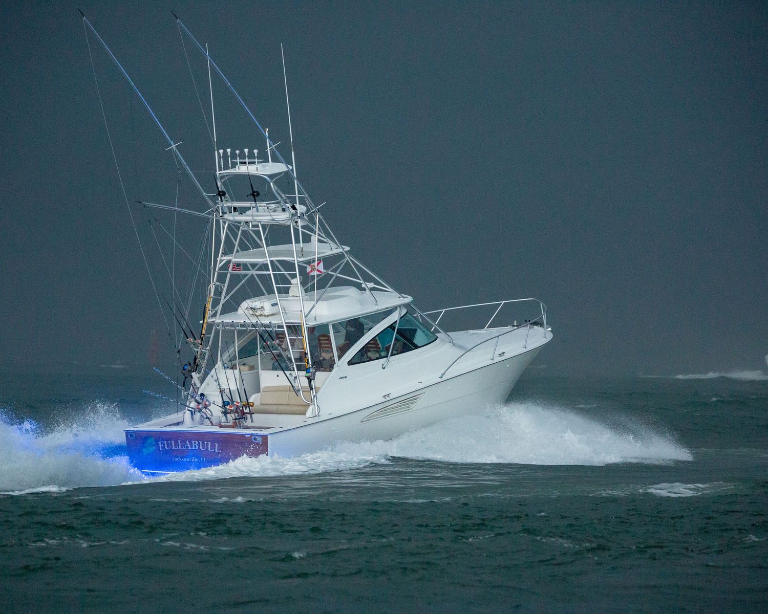 White sport fishing vessel creates dramatic spray while navigating stormy seas at dusk.