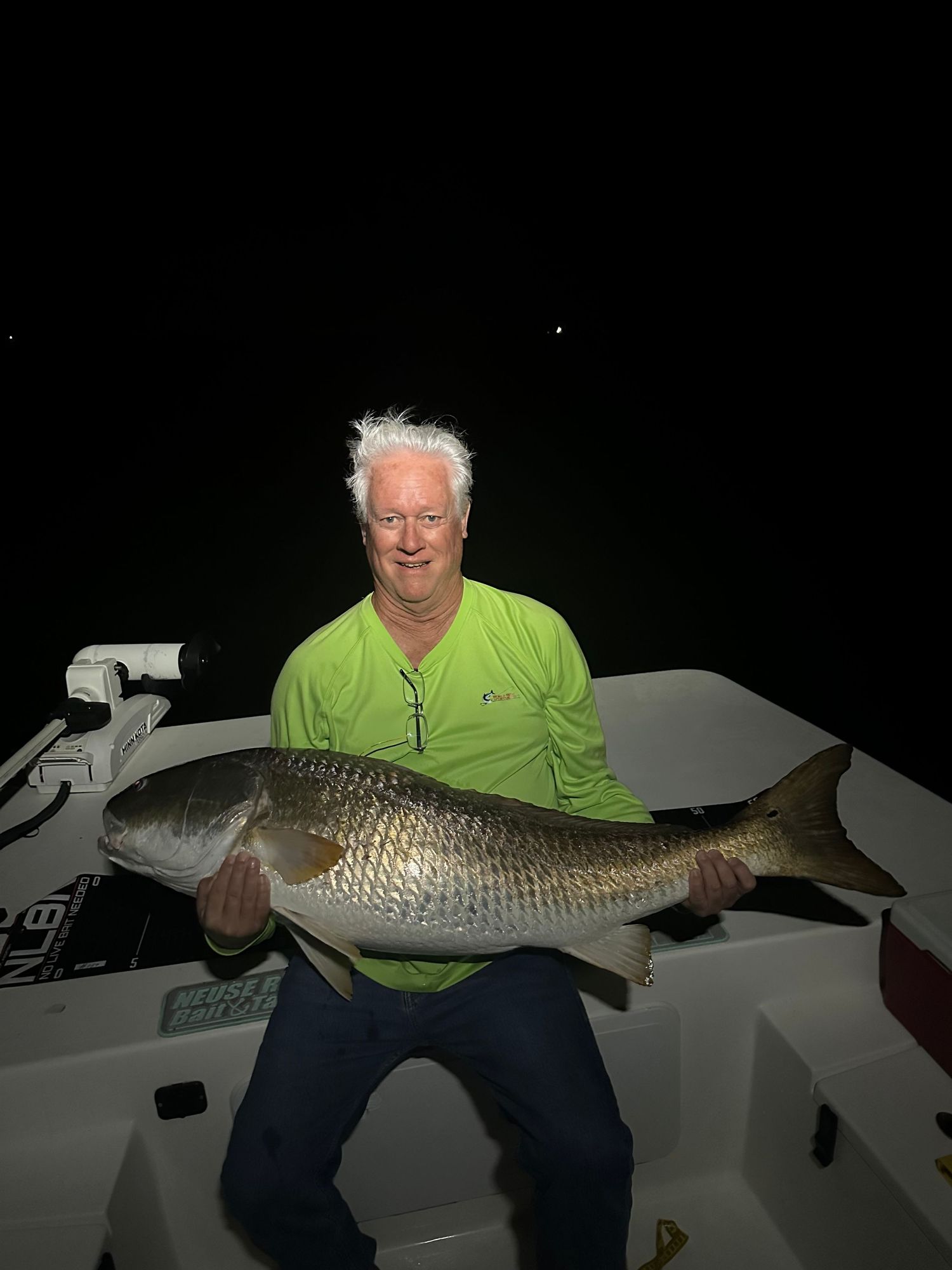 Large redfish catch being displayed at night on boat deck with fishing equipment visible.