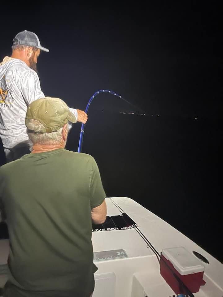 Seasoned angler patiently holds fishing rod while night fishing on a boat deck.