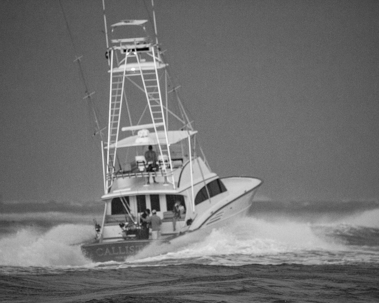 Sport fishing vessels power through stormy seas in black and white photography.