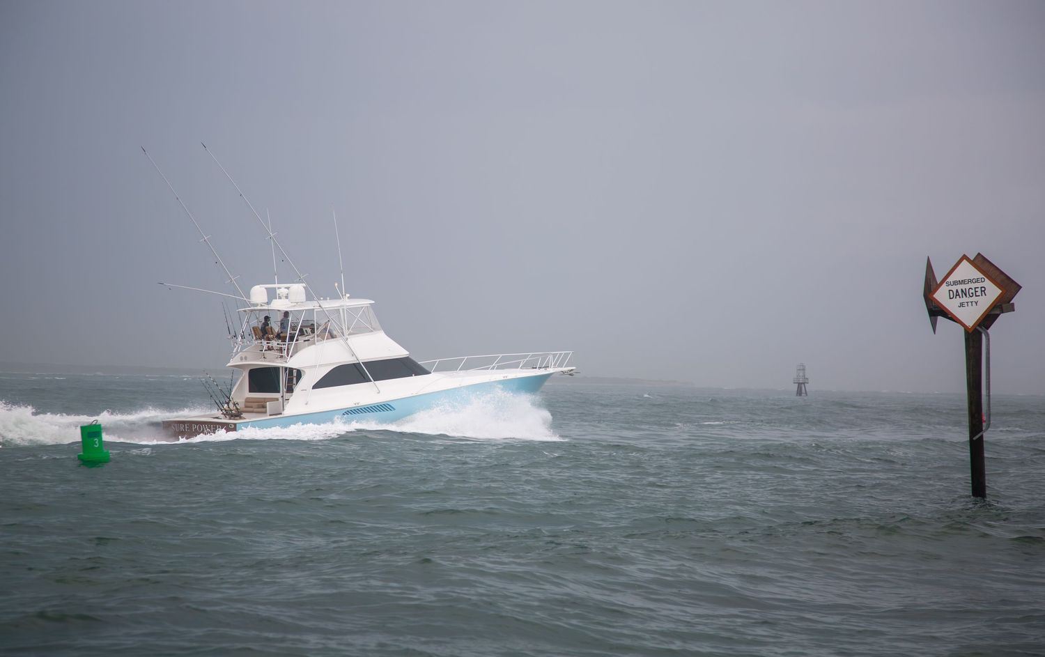 White sport fishing yacht passes navigation markers in stormy conditions.