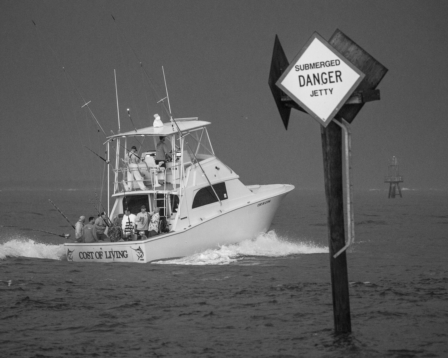 Black and white image of a sport fishing boat passing a danger marker in rough seas.