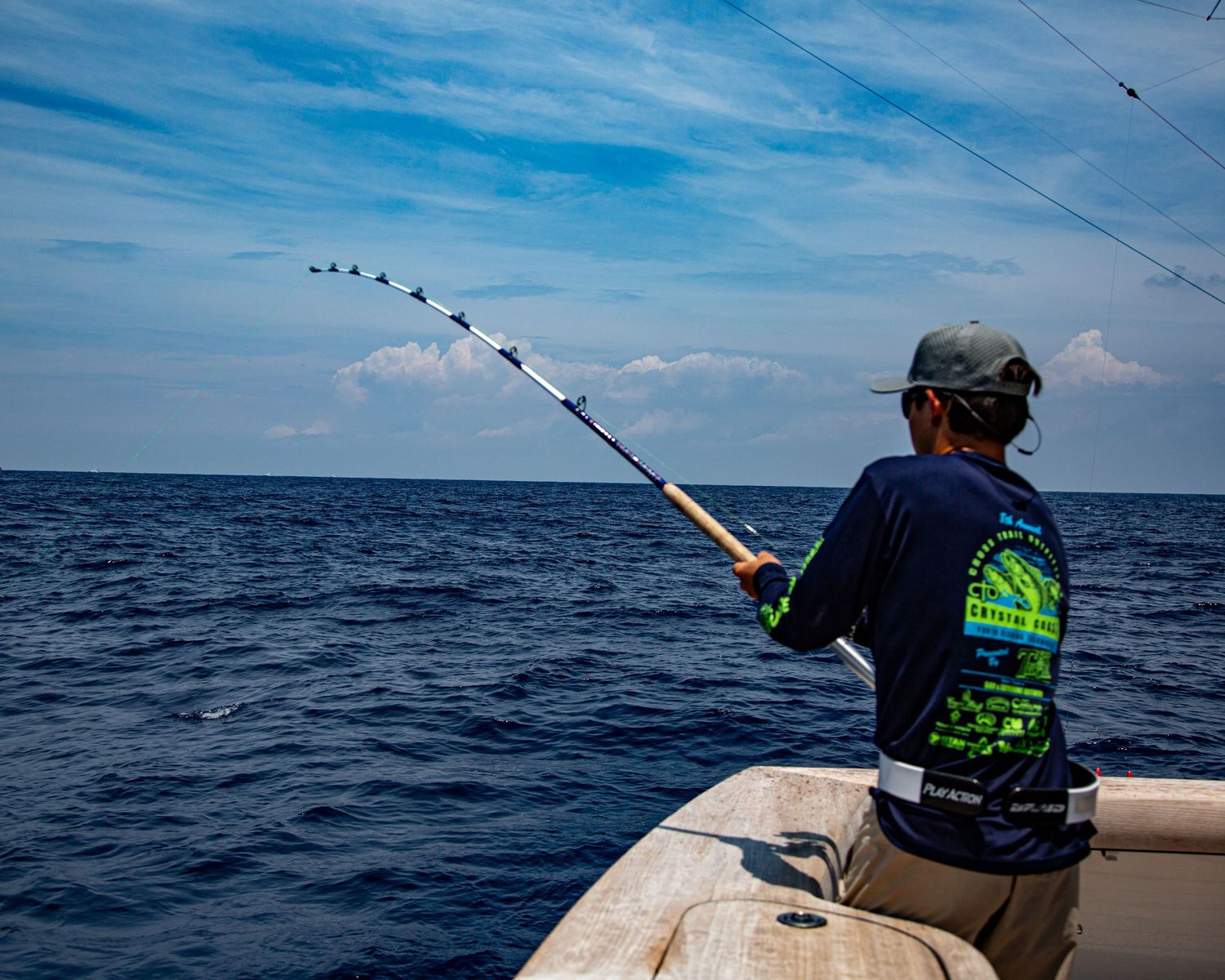 A angler fishing from a boat on calm ocean waters under a partly cloudy blue sky.