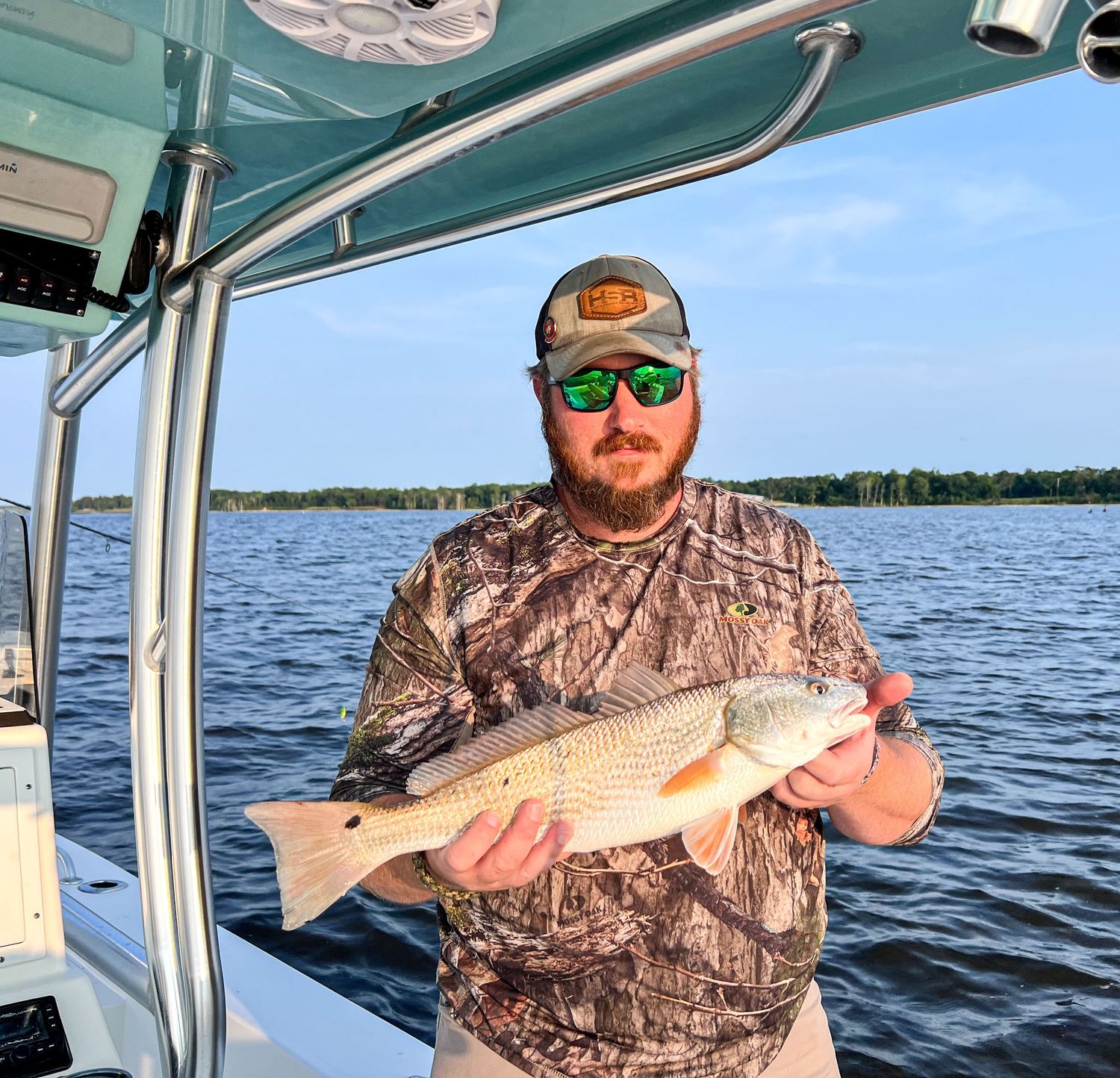 Angler in camo shirt displays redfish catch on boat deck.