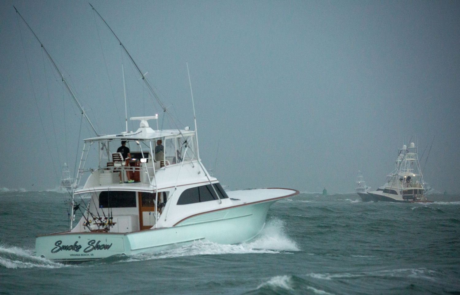 Multiple sport fishing boats cruising in formation through choppy waters.