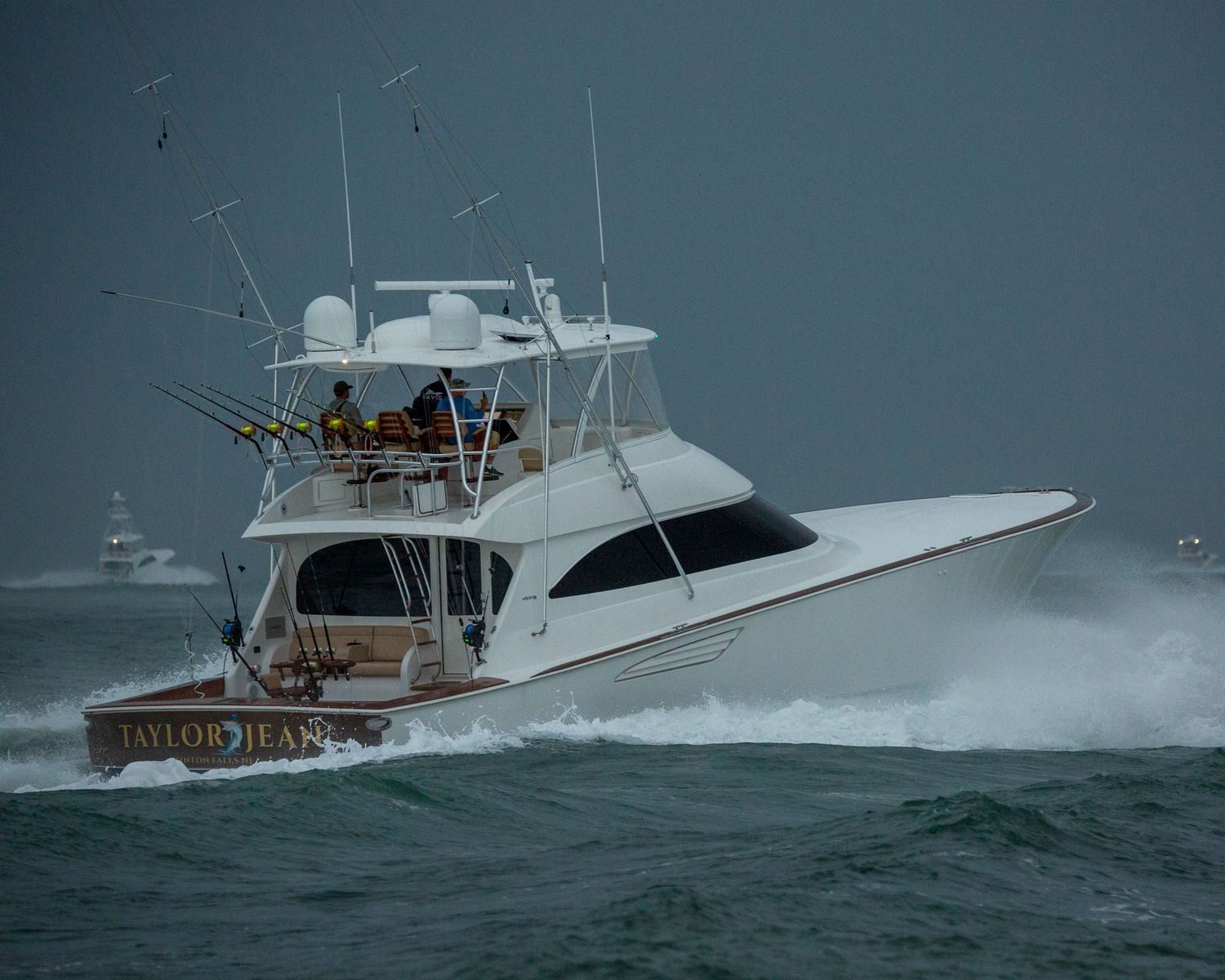 White sport fishing yacht powering through rough ocean waves with spray flying.