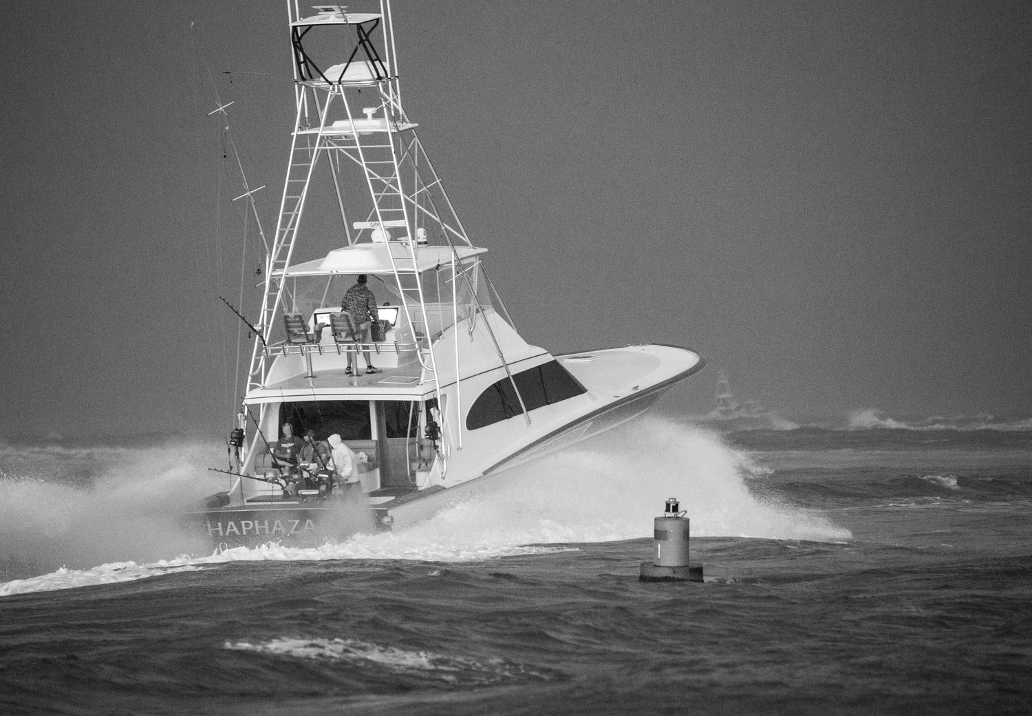 Sport fishing boat crashes through large ocean waves in rough seas, creating dramatic white spray.