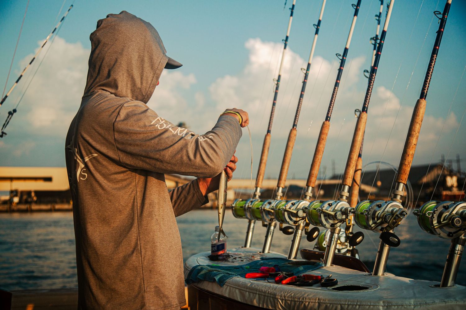 Angler in hooded jacket preparing fishing rods on a boat dock at sunset.