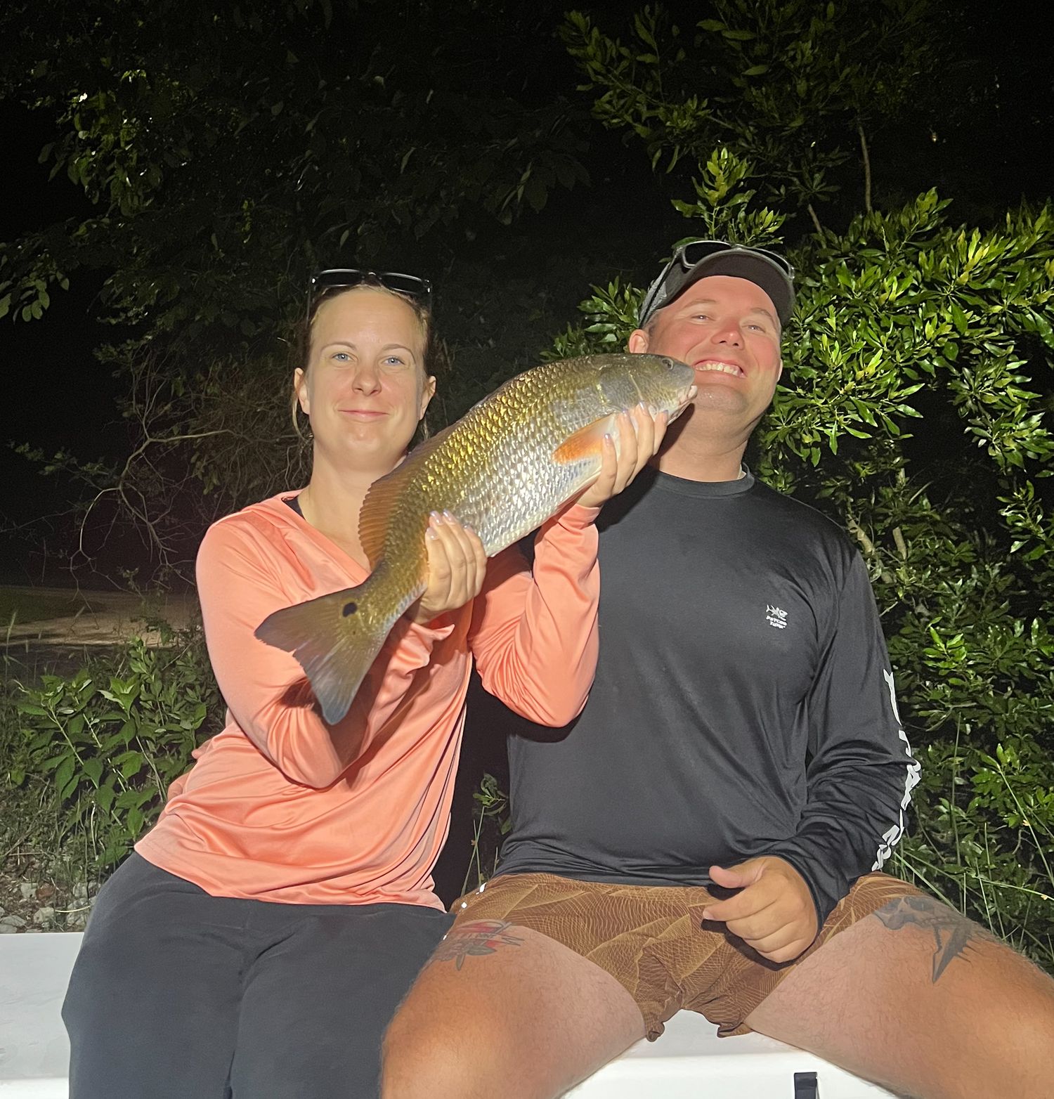 Two anglers proudly display a large common carp caught during a nighttime fishing trip outdoors.