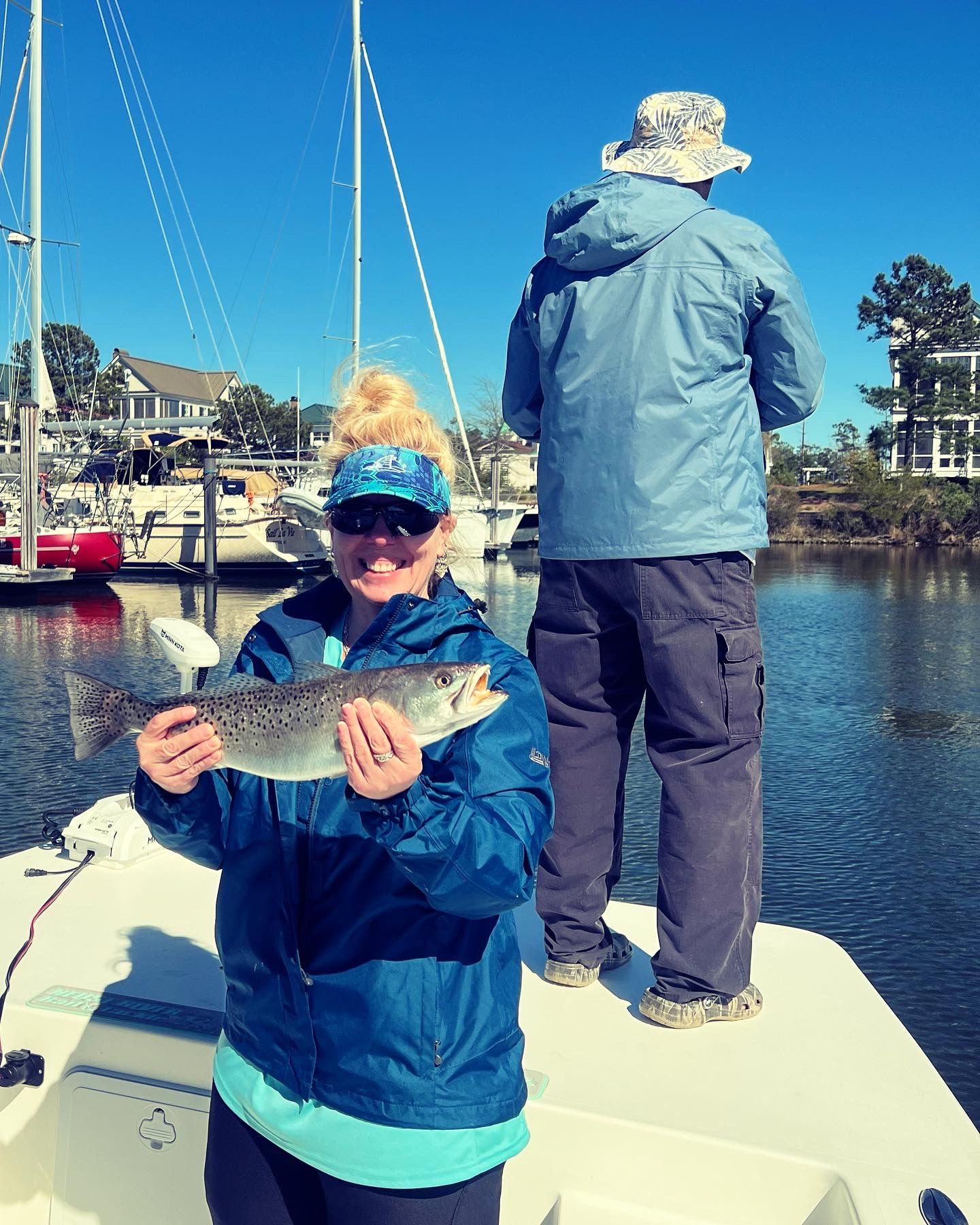 Several fish catches being displayed on a boat deck with marina and blue sky in background.