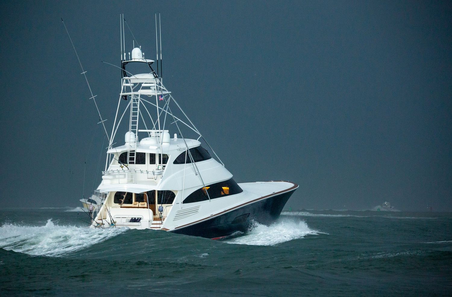 White sportfishing yacht powering through rough seas with spray flying.