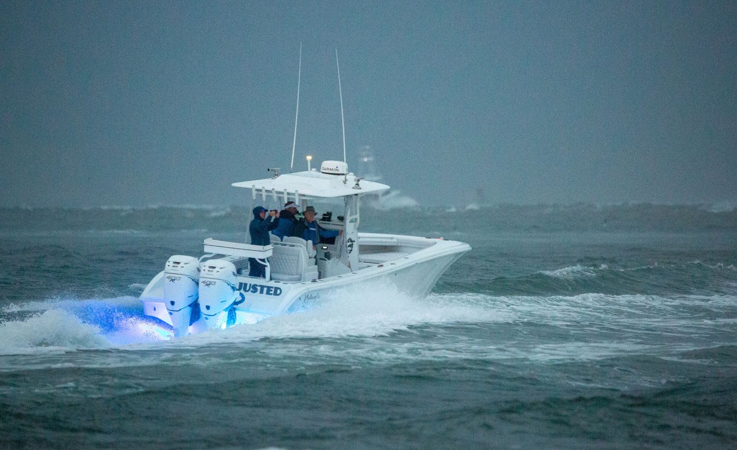 White sport fishing vessel crashes through stormy waves in rough conditions.