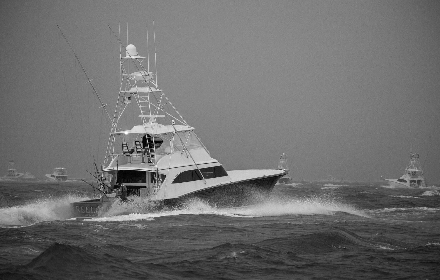 Deep sea fishing vessels plowing through stormy ocean waves in black and white.